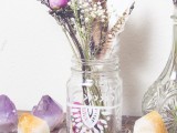 a glass jar with tribal patterns, dried and fresh blooms and feathers for a boho summer wedding