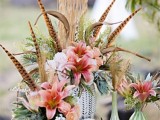 a bright pink wedding centerpiece with much greenery and feathers is a great boho wedding idea