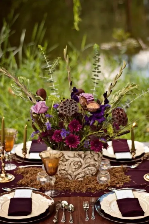a refined and elegant dark bloom wedding centerpiece with lotus flowers, greenery and feathers for a moody boho wedding