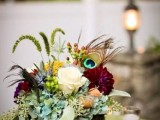 a colorful and quirky wedding centerpiece with greenery, blooms, herbs and peacock feathers