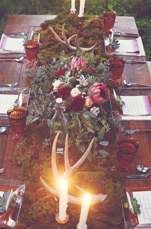 a lush boho wedding centerpiece composed of moss, antlers, greenery, succulents, pink and white blooms and berries