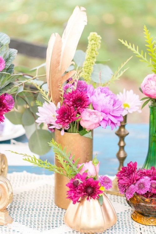 bright floral centerpieces with feathers placed into gilded vases and candles for a bright boho wedding