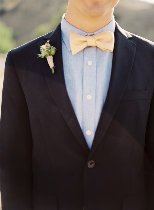 a black suit, a chambray shirt and a yellow bow tie plus a pastel floral boutonniere for a stylish look