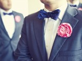 a grey suit with a navy polka dot bow tie and a pink bloom boutonniere is a chic option to rock on your big day