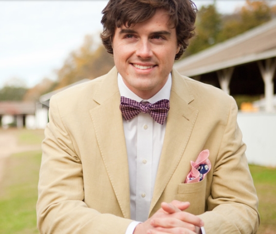 A tan suit, a white shirt, a pink printed bow tie and a colorful handkerchief for a stylish summer groom's look