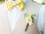 a bright summer groom’s look with a white shirt, a tan waistcoat, a yellow and white striped bow tie and a bright boutonniere