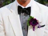 a white suit, a printed grey shirt, a black bow tie and a purple boutonniere that brings color to this monochrome
