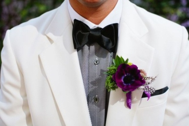 A white suit, a printed grey shirt, a black bow tie and a purple boutonniere that brings color to this monochrome