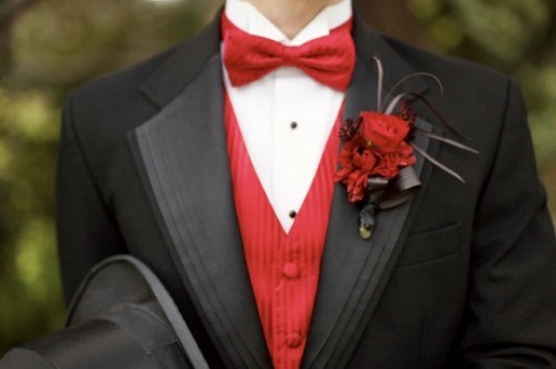 a black tux, a red waistcoat, a red bow tie and a bold floral boutonniere for a refined and vintage-inspired groom's look