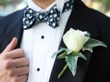 a black tux, a white shirt with black buttons, a black and blue printed bow tie and a white rose boutonniere for pure elegance
