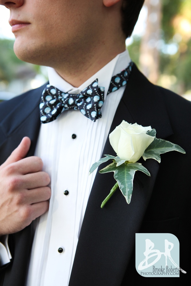 A black tux, a white shirt with black buttons, a black and blue printed bow tie and a white rose boutonniere for pure elegance