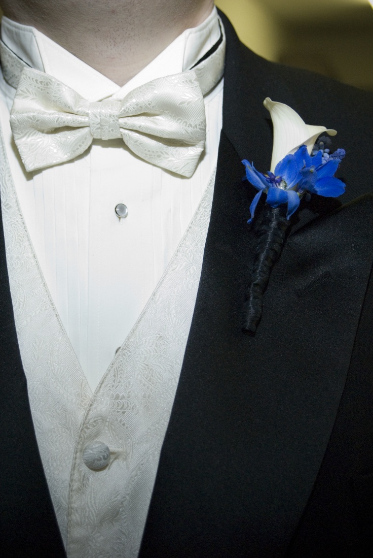 A morning suit with a white waistcoat and a matching bow tie and a white and blue floral boutonniere for an elegant touch