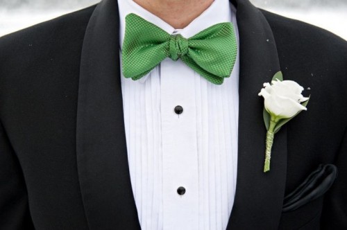 a black tux, a white shirt with black buttons, an apple green bow tie and a neutral floral boutonniere for an elegant and refined look