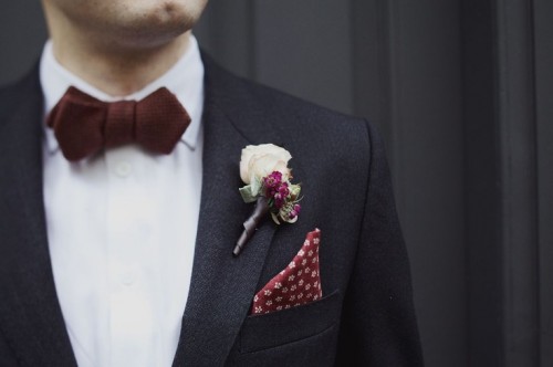 a black suit, a chocolate bow tie, a white floral boutonniere and a printed handkerchief for a refined and chic look in the fall or winter