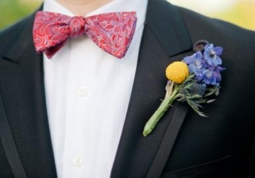 a black tux, a printed pink bow tie, a colorful floral boutonniere that refreshes and accents the look