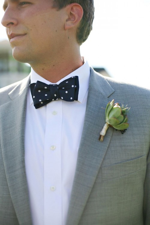 a grey suit, a navy polka dot bow tie and a succulent boutonniere for an elegant and modern look