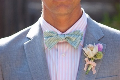 a grey suit highlighted with a pink and white striped shirt and a printed colored bow tie plus a floral boutonniere