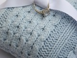 a blue cable knit ring pillow with a white ribbon is a lovely accessory for a winter wedding, you can make it yourself