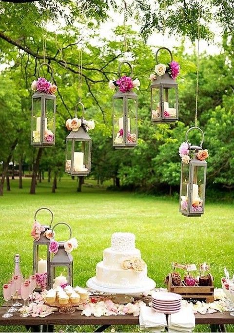 a sweets table with pink blooms and candle lanterns decorated with blooms over it and with delicious sweets and pink champagne