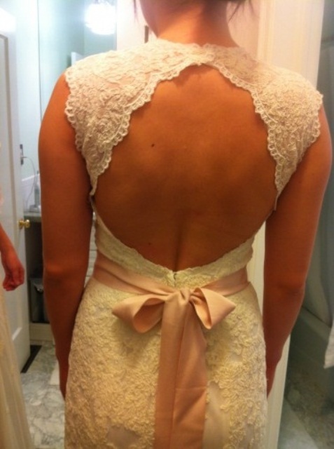 a vintage lace fitting wedding dress with no sleeves, a high neckline, a keyhole back and a pink sash with a bow on the back