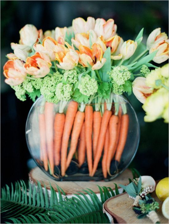 a round jar with orange tulips and fresh greenery and fresh carrots to decorate the jar inside