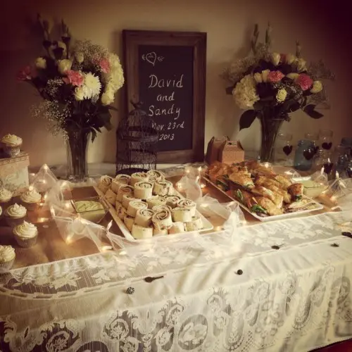 a refined vintage dessert table with floral arrangements, with cupcakes, sweets and other stuff and a chalkboard with the menu