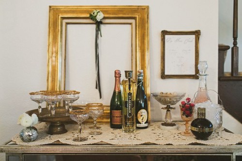 a small and chic drink table for a vintage bridal shower, with champagne and gold-rimmed glasses plus blooms in round vases