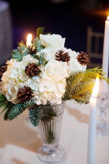 a simple and cute winter bridal shower centerpiece of white blooms, pinecones, evergreens in a large glass