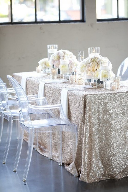 a glam winter bridal shower tablescape with a sequin tablecloth, white floral centerpieces and pillar candles