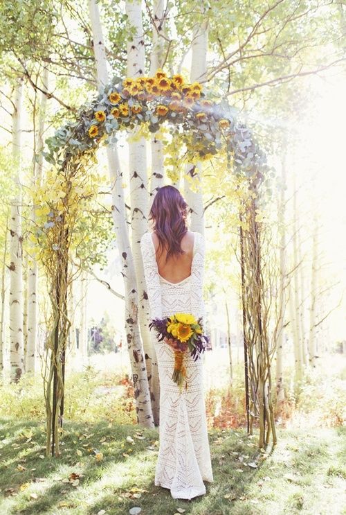 a rustic woodland wedding arch of branches and twigs, with pale foliage and sunflowers on top is lovely and bright
