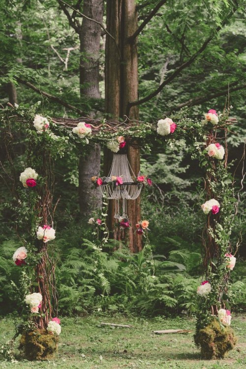a bright woodland wedding arch of branches and twigs, with greenery and leaves, white and bright pink blooms and moss at the base
