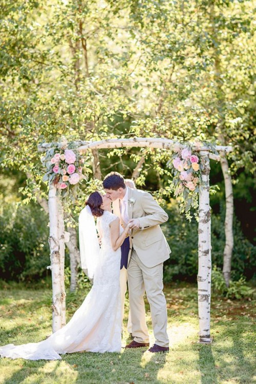 a rustic woodland wedding arch of birch branches, pale greenery, white and pink blooms is a simple and stylish idea with a rustic feel