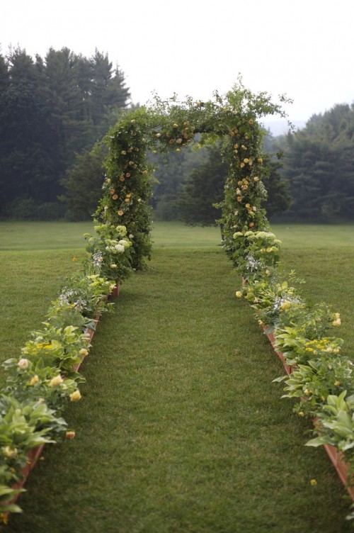 a cool woodland wedding arch fully covered with greenery and bold yellow blooms and with a forest view is fantastic