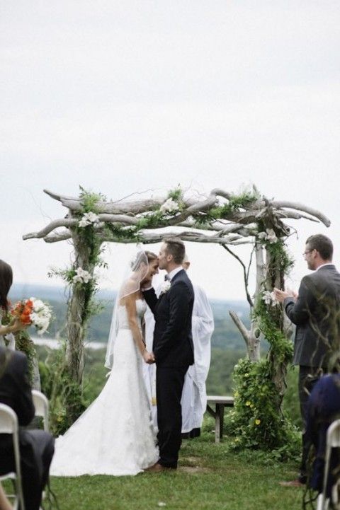 a wild woodland wedding arch of branches, with greenery and white blooms and a cool view of the valley