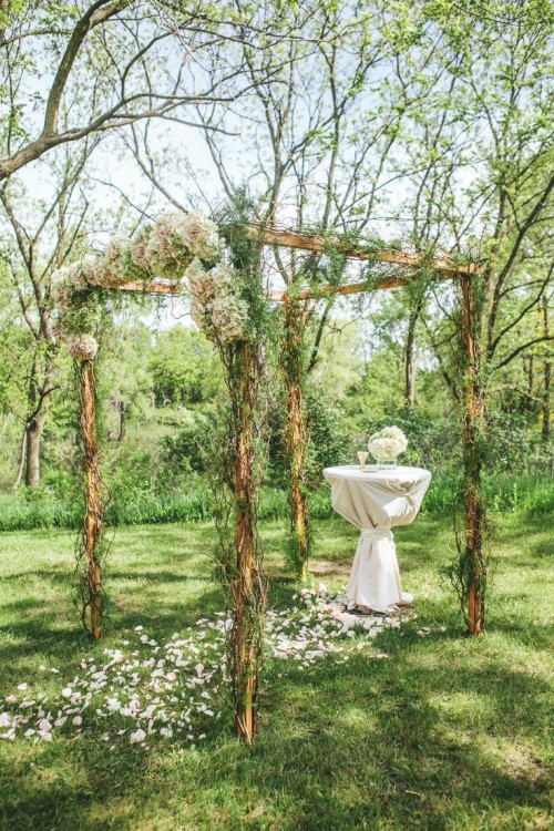a romantic woodland wedding arch of branches and twigs, with greenery and pastel blooms and petals inside for a spring or summer wedding