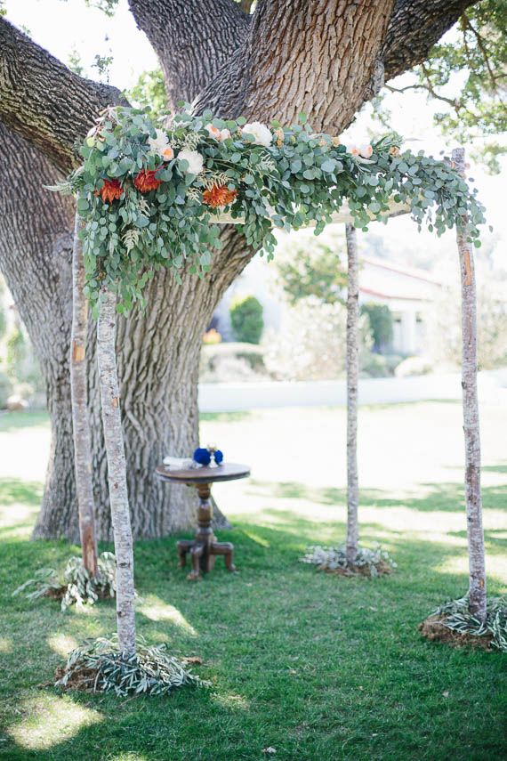 A woodland wedding arch of branches, with greenery, pastel and bold blooms and greenery at the base