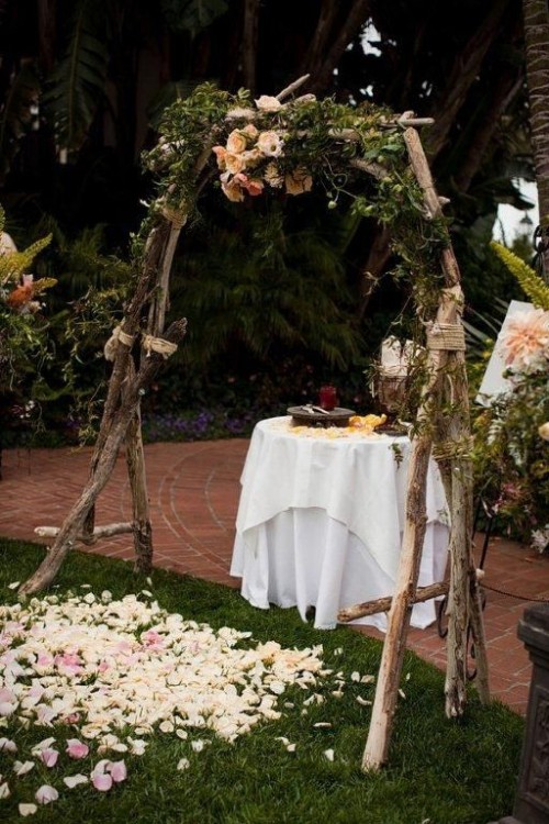 a branch wedding arch with twine, greenery and pastel blooms and some petals on the ground is very cool