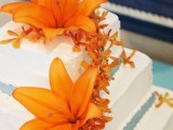 a white square wedding cake styled with blue ribbon and bold orange blooms looks very tropical and bold and will fit a beach wedding easily