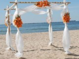 a lovely beach wedding arch with white curtains and orange blooms is a stylish idea for an orange beach wedding