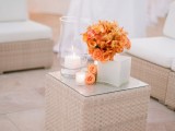 a chic white wedding lounge with wicker furniture, white curtains and a bright orange bloom centerpiece for an orange beach wedding
