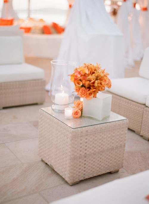 a chic white wedding lounge with wicker furniture, white curtains and a bright orange bloom centerpiece for an orange beach wedding