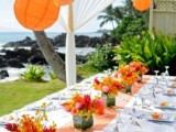 a bold and cool orange beach reception space with orange paper lamps and blooms, an orange table runner and white porcelain is super cool