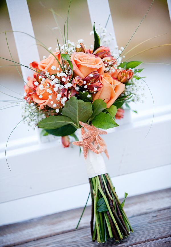 An orange bloom wedding bouquet with baby's breath and leaves plus a white wrap is a cool idea for an orange beach wedding