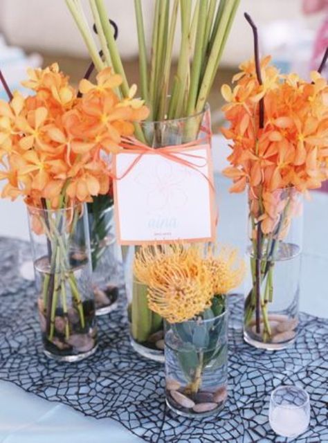 a bright orange wedding centerpiece with lots of various blooms in vases, with a ribbon and a tag is a very cool beach wedding idea