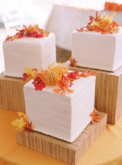 square white wedding cakes with orange and yellow blooms and petals on top are amazing for a beach or tropical wedding