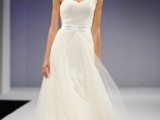 a modern wedding ballgown with a one shoulder neckline, a layered skirt and a small hat with fabric blooms for a refined look