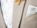 a formal beach groom’s outfit with a tan suit, a white waistcoat, a white tie and a little star fish boutonniere
