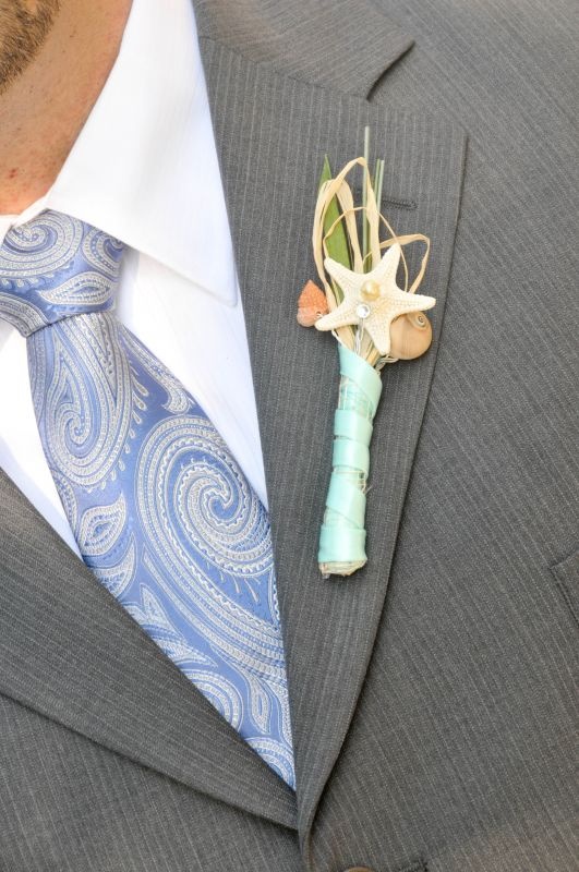 a light grey suit, a blue printed tie and a colorful boutonniere