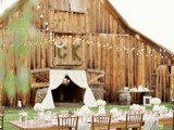 an outdoor barn reception space with long tables, white floral arrangements and string lights over the space