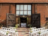 an outdoor barn wedding ceremony space with a greenery arch, simple chairs decorated with greenery and blooms is a cool space